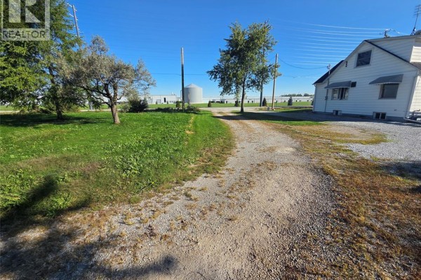 Gravel driveway leading towards a white house with agricultural buildings in distance. - 618 Mersea Road 8, Leamington