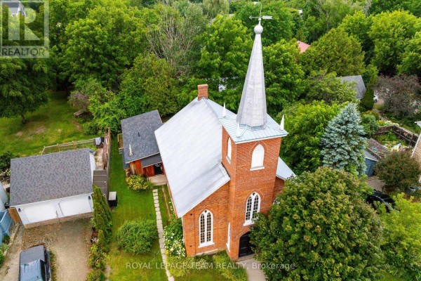 Aerial view of a red brick church with a silver steeple and metal roof surrounded by trees. - 618 St. Lawrence Street, Merrickville Wolford