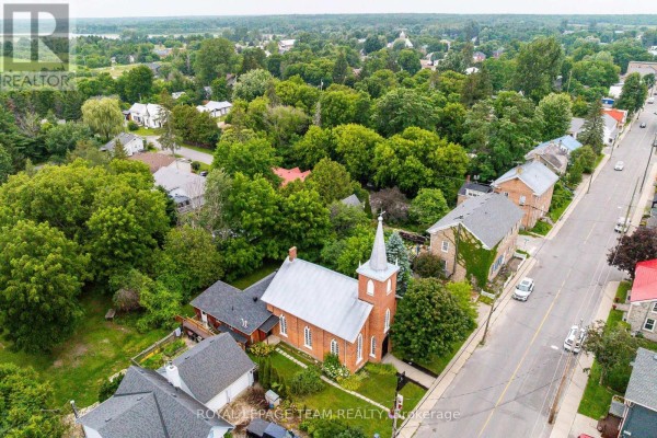 Aerial view of the church property, showing surrounding homes, trees, and the Rideau River in the distance. - 618 St. Lawrence Street, Merrickville Wolford