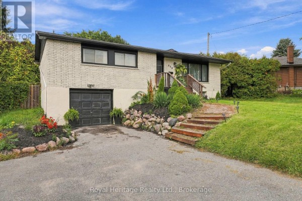 Side view of a white brick house with a black garage door, driveway, and landscaping. - 618 Sunset Boulevard, Clarington