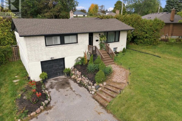 Aerial view of a white brick house with a black garage door, paved driveway, and green lawn. - 618 Sunset Boulevard, Clarington