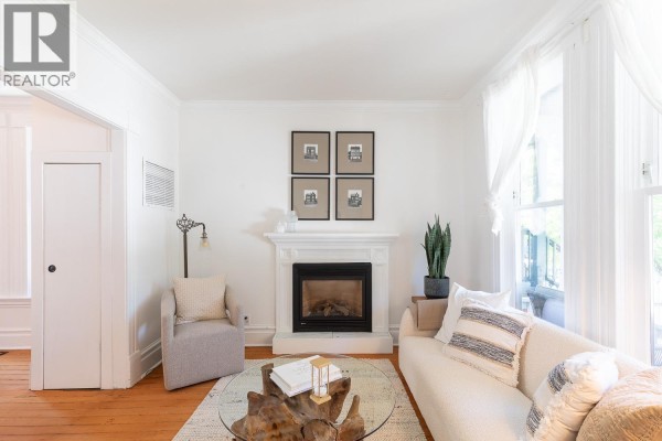 Living room with a white fireplace, sofa, armchair, coffee table, and large windows with white curtains. - 618 Union Street, Vancouver