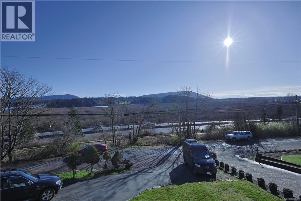 View of a landscape with hills, trees, a road, and parked cars under a sunny sky. - 6180 Alington Rd, Duncan