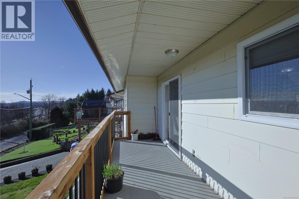 A wide wooden deck with black railings overlooks a sloped lawn and distant town. - 6180 Alington Rd, Duncan