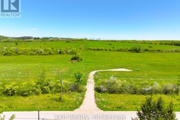 Gravel driveway leads through a green field towards a line of trees under a blue sky. - 618129 Grey Road 18, Meaford