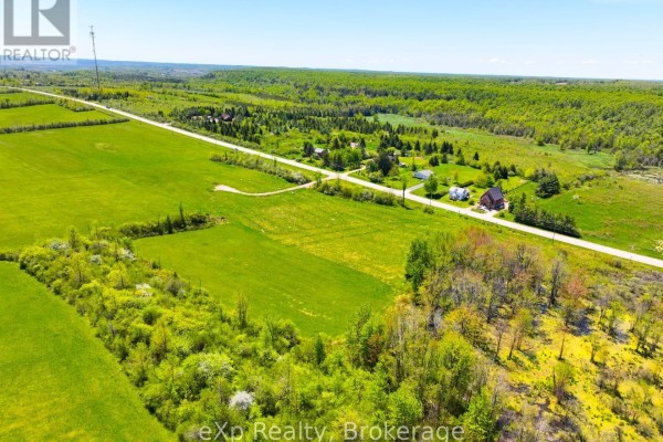 Aerial view showing a paved road, houses, green fields, and dense trees on rolling terrain. - 618129 Grey Road 18, Meaford