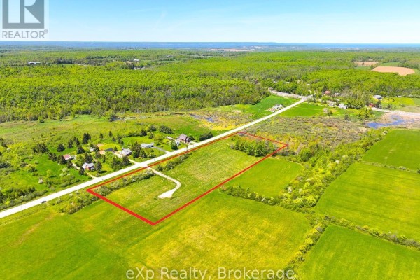 Aerial view of a property outlined in red, featuring green fields, trees, and a paved road. - 618129 Grey Road 18, Meaford