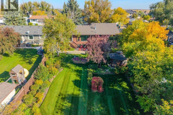 Aerial view of the backyard with a lush lawn, mature trees, a wooden deck, a gazebo, and a children's play structure. - 619 Clover Avenue, Dalmeny