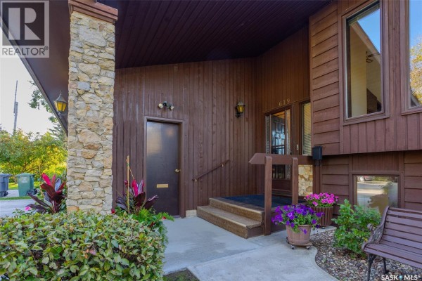 Close-up of the covered front entrance with stone pillars, wood siding, steps, and potted plants. - 619 Clover Avenue, Dalmeny