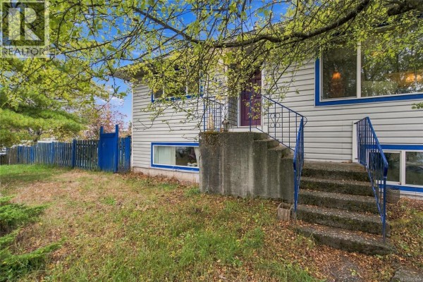 Front exterior of a grey house with blue trim, showing concrete steps and a blue wooden fence. - 619 Pine St, Nanaimo