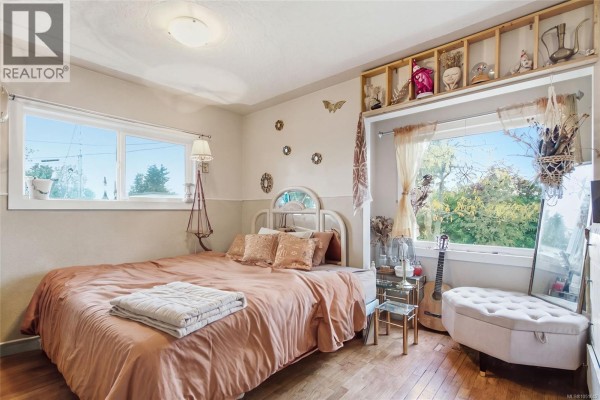 Bedroom with a queen-size bed, large window, wooden floors, and decorative shelving above the window. - 619 Pine St, Nanaimo