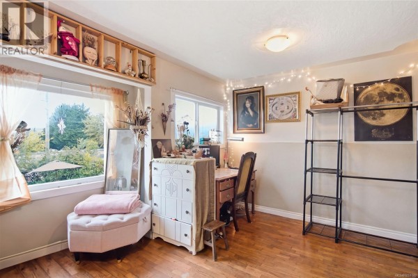 Second bedroom with a desk, chair, storage shelves, and a large window overlooking the backyard. - 619 Pine St, Nanaimo