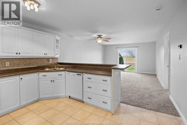 Backyard with green grass, paved patio, fenced yard, and view of a running track and stadium. - 619 Rodfam, Windsor