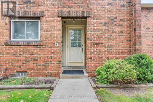 Front door of a townhouse with a concrete walkway and small bushes. - 62 - 201 Silvercreek Parkway N, Guelph