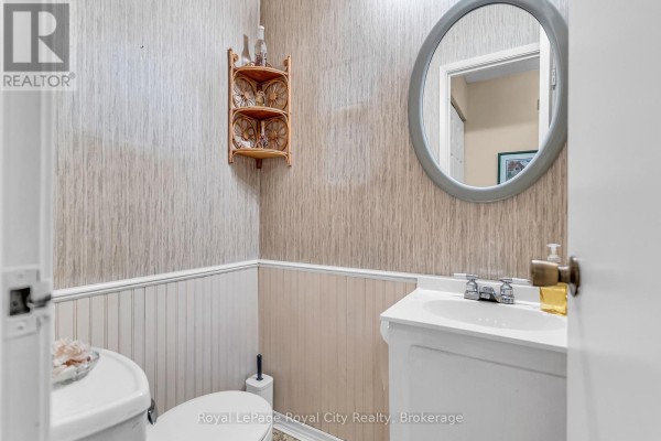 Small half bathroom with a toilet, vanity, and mirror with textured wallpaper. - 62 - 201 Silvercreek Parkway N, Guelph