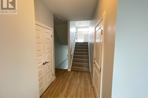 Interior hallway with light wood laminate flooring, white doors, and carpeted stairs leading up. - 62 - 819 Kleinburg Drive, London North