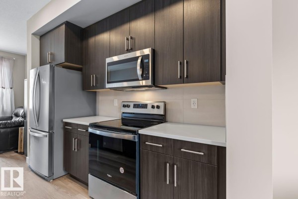 Kitchen area featuring dark cabinetry, stainless steel appliances, and white countertops - #62 13139 205 St Nw, Edmonton