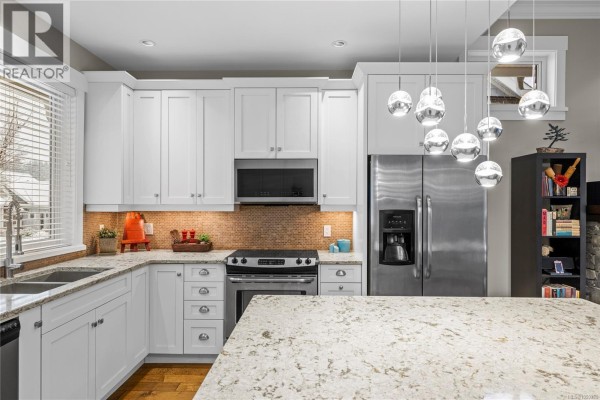 Kitchen with white cabinets, pendant lighting, and a view of the backyard. - 62 5251 Island Hwy W, Qualicum Beach