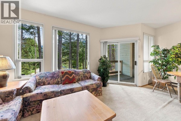 Living room with patterned sofa, large windows offering a forest view, and a sliding glass door. - 62 6127 Eagleridge Crescent, Whistler