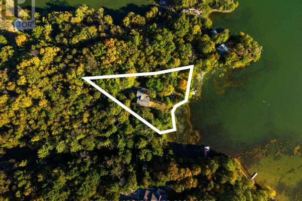 Aerial view of a large waterfront property with a home surrounded by trees and bordering a green lake. - 62 Apple Jack Lane, Frontenac
