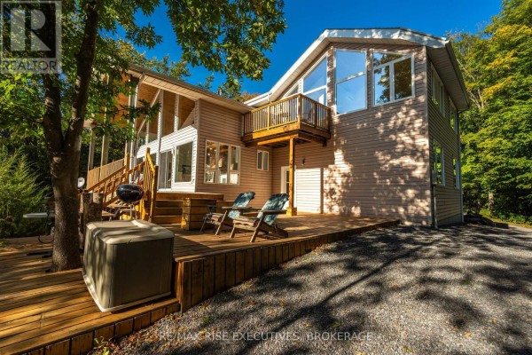 Expansive wooden deck with hot tub, grill, and chairs leading to a modern tan-sided home. - 62 Apple Jack Lane, Frontenac