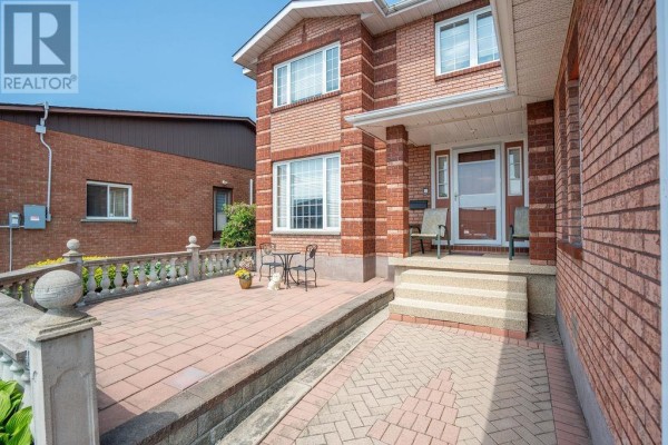 Close-up of the front entrance patio area with brick pavers, stone railing, and a small bistro set. - 62 Bitonti Cres, Sault Ste  Marie