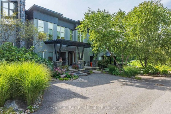 Modern townhouse entrance with gray siding, large windows, and lush landscaping. - 62 Carrick Trail, Gravenhurst)