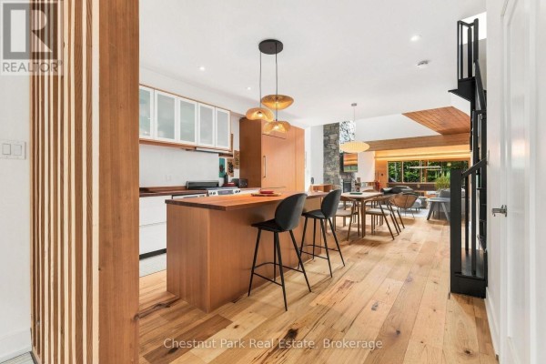 Open-concept kitchen and dining area with a wooden island, modern chairs, and light wood floors. - 62 Carrick Trail, Gravenhurst)