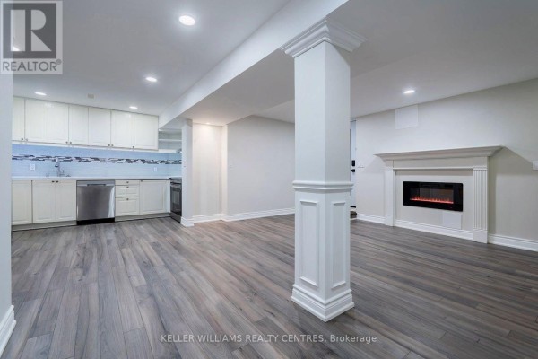 Unfinished basement with white cabinets, stainless steel appliances, and a decorative fireplace. - 62 Corner Ridge Road, Aurora