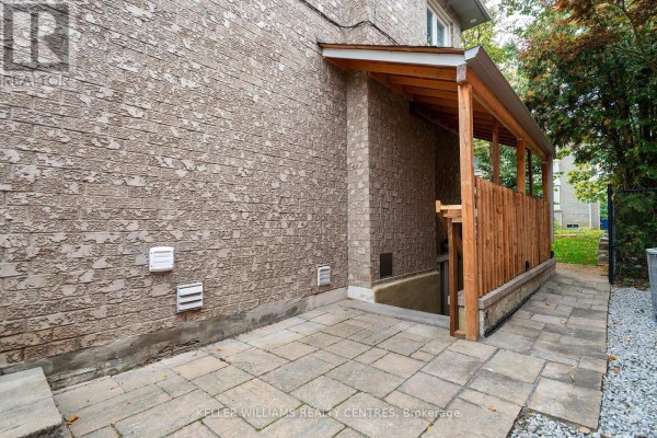 Outdoor stone patio leading to a wooden covered staircase descending into a basement entrance. - 62 Corner Ridge Road, Aurora