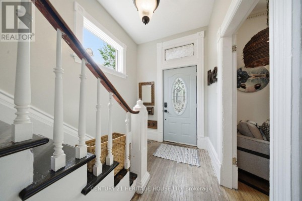 Living room featuring a white brick fireplace, two yellow upholstered chairs with a white faux fur throw, and a large wooden cabinet. - 62 East Avenue, Brantford
