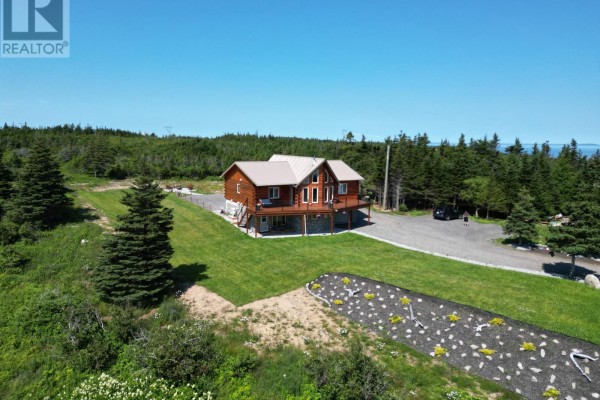 View of the log home from the side, with a gravel driveway, green lawn, trees, and a white SUV. - 62 Front Road, Port Au Port West