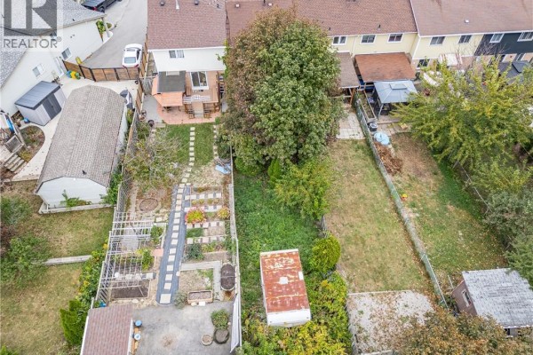 Aerial view of townhouse backyards, featuring patios, gardens, sheds, and green space. - 62 Gledhill Crescent, Hamilton