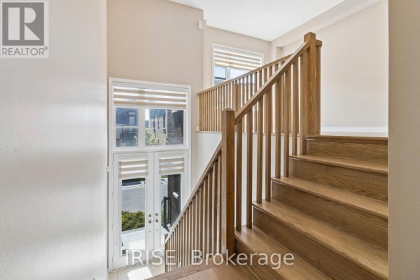 Interior view of a wooden staircase and railings with large windows and blinds overlooking the entrance. - 62 Laskin Drive, Vaughan