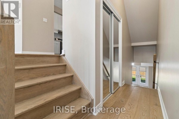 Hallway with light wood floors, a wooden staircase, and mirrored closet doors leading to a rear exit. - 62 Laskin Drive, Vaughan