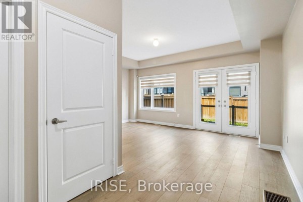Living area with light wood floors, a white door on the left, and double doors leading outside. - 62 Laskin Drive, Vaughan