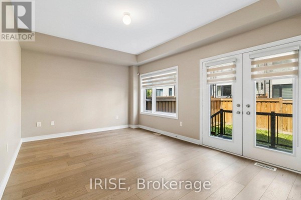 Living room with light wood floors, beige walls, and double glass doors opening to a backyard patio. - 62 Laskin Drive, Vaughan
