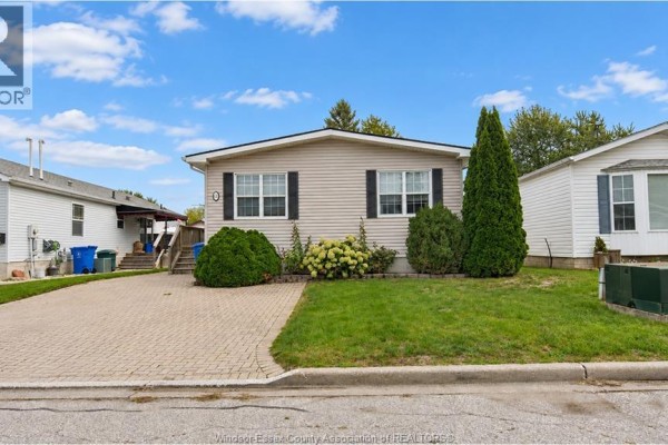 Exterior view of the beige modular home with a paved driveway and surrounding landscaping. - 62 Malden Hill Drive, Amherstburg