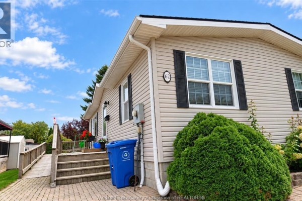 Close-up of the beige siding and windows of the modular home with a blue bin. - 62 Malden Hill Drive, Amherstburg