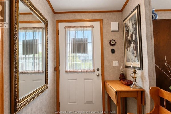 Interior entryway with a white door, large mirror, wooden console table, and framed artwork. - 62 Malden Hill Drive, Amherstburg