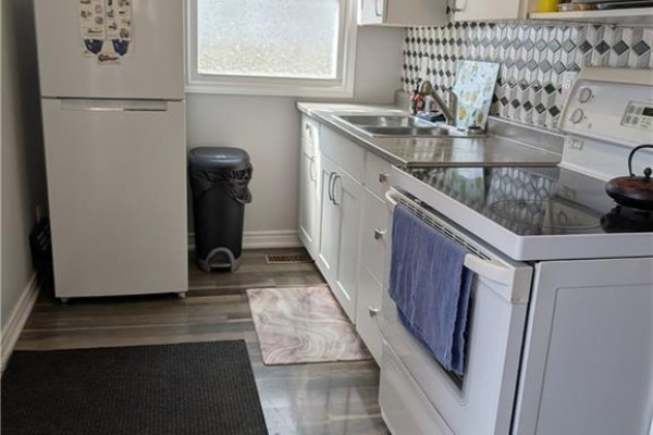 Kitchen with white cabinets, tile backsplash, and dark wood-look flooring - 62 Ninth Avenue Brantford