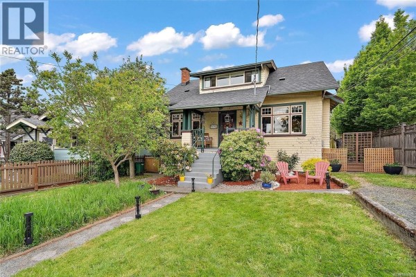 Front view of a two-story yellow house with a paved driveway and lush greenery. - 62 Obed Ave, Saanich