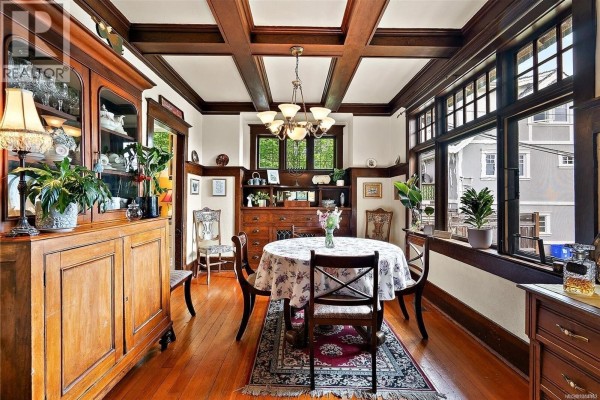 Dining room with a round table, floral tablecloth, wooden chairs, and a large china cabinet. - 62 Obed Ave, Saanich