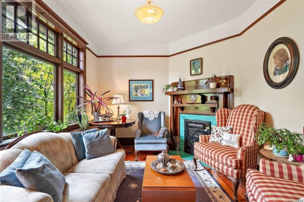 Living room with a bay window, fireplace with turquoise tiles, and patterned armchairs. - 62 Obed Ave, Saanich