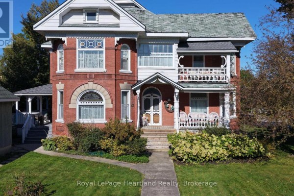 Front view of a red brick house with a white porch, balcony, and manicured lawn. - 62 Orange Street S, Central Huron