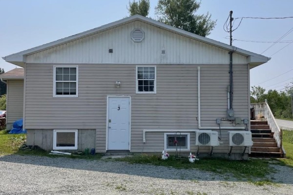 The back exterior of the beige vinyl-sided house showing the door and outdoor air conditioning units. - 62 Timmons Maclean Road, Newtown