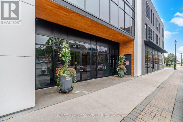 Building entrance with large glass doors, wood accents, and potted plants on the sidewalk. - 620 - 185 Dunlop Street E, Barrie
