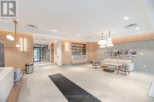 Lobby with light wood paneling, a bar area, grey sofa, chairs, and contemporary lighting fixtures. - 620 - 185 Dunlop Street E, Barrie