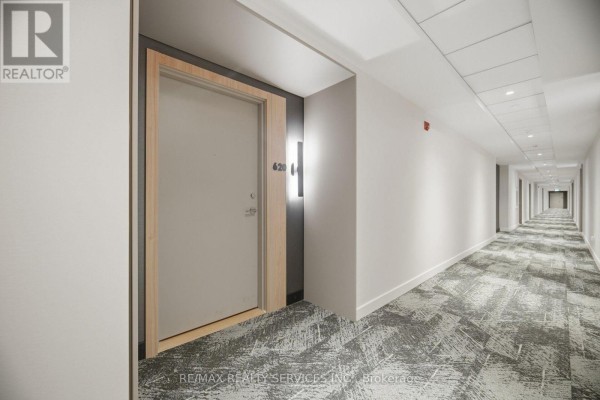 Apartment hallway with light grey walls, wood trim around a door labeled 620, and patterned carpet. - 620 - 185 Dunlop Street E, Barrie