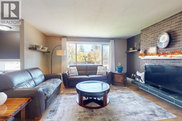 Spacious living room featuring a brick fireplace, large window, two leather sofas, and a patterned area rug. - 620 Ziprick Road, Kelowna